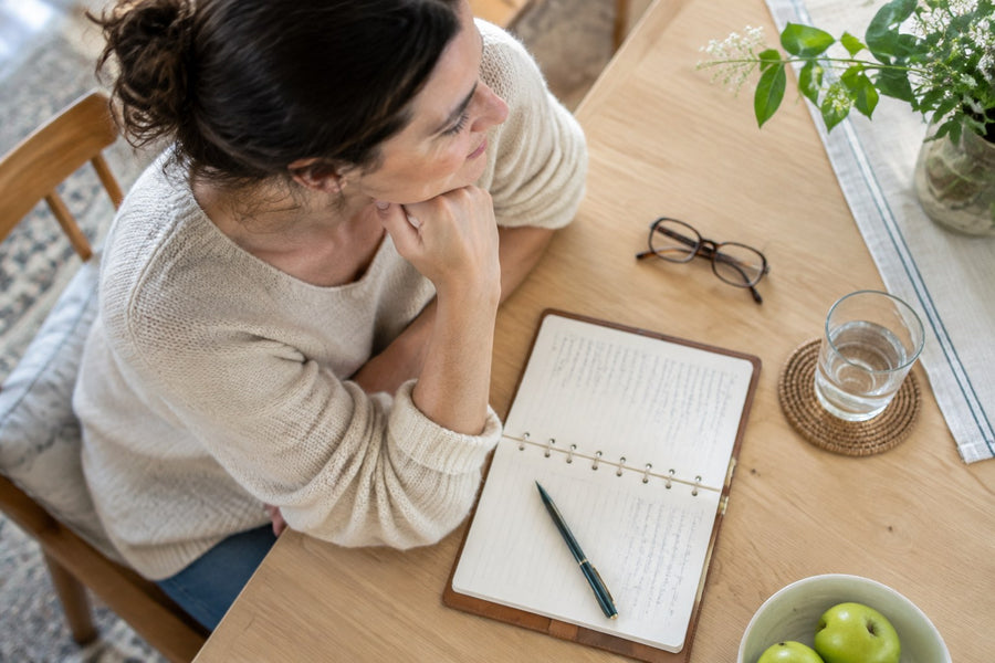 An open notebook, reading glasses and a glass of water on a wooden table